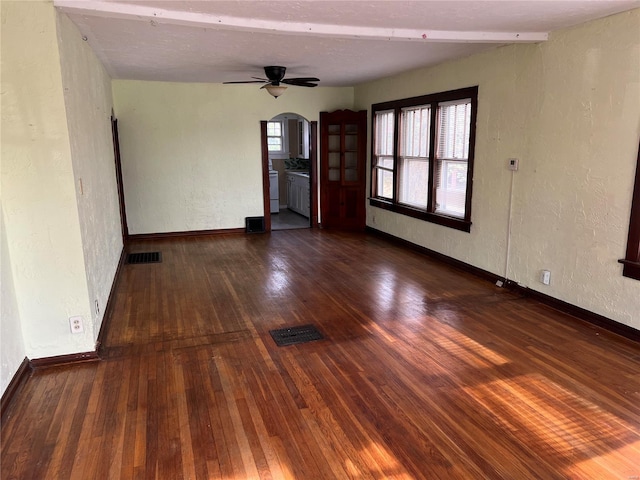 empty room featuring arched walkways, a textured wall, hardwood / wood-style flooring, and visible vents