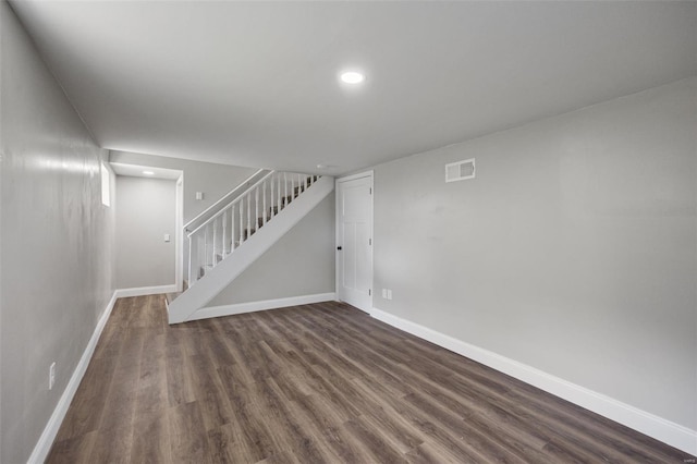 finished basement with visible vents, baseboards, dark wood-type flooring, and stairs