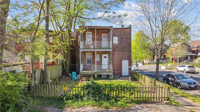 townhome / multi-family property with a chimney, a balcony, brick siding, and a fenced front yard