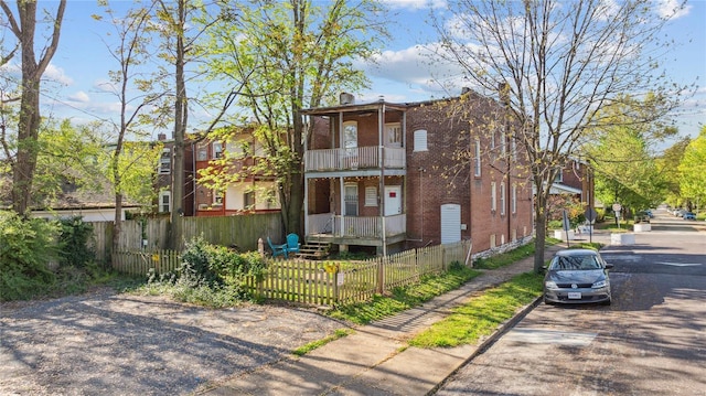 exterior space with brick siding, a balcony, and a fenced front yard