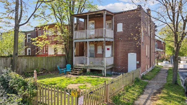 back of house with brick siding, a fenced backyard, and a balcony
