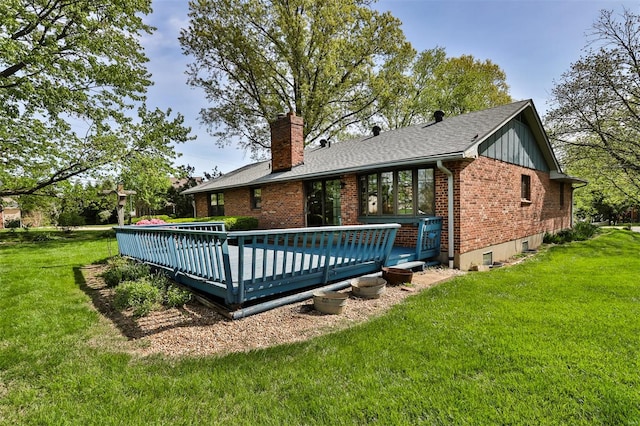 rear view of house featuring roof with shingles, a chimney, brick siding, a deck, and a yard