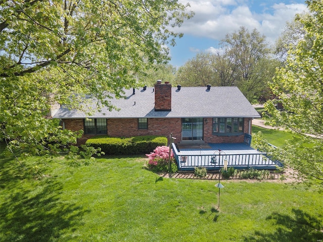 rear view of house featuring a lawn, a chimney, a wooden deck, brick siding, and roof with shingles