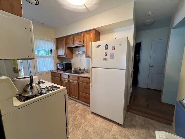 kitchen with a sink, light countertops, brown cabinetry, and white appliances