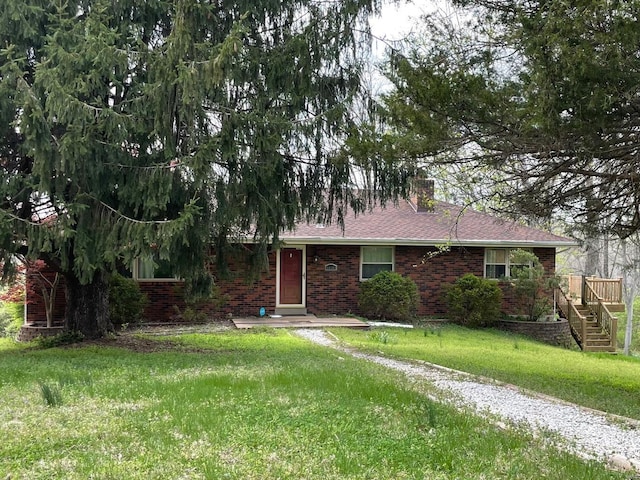ranch-style home with a chimney, a shingled roof, a front yard, brick siding, and stairs