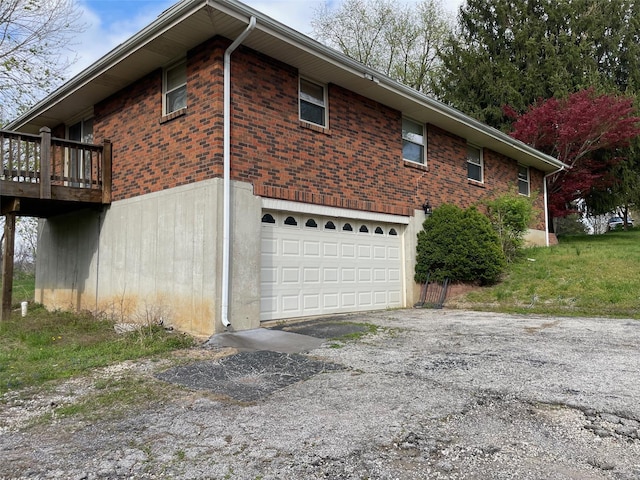 view of side of home featuring an attached garage, a wooden deck, aphalt driveway, and brick siding