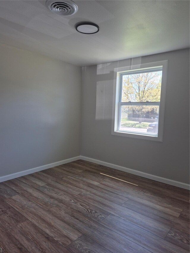 unfurnished room featuring baseboards, dark wood-style flooring, and visible vents