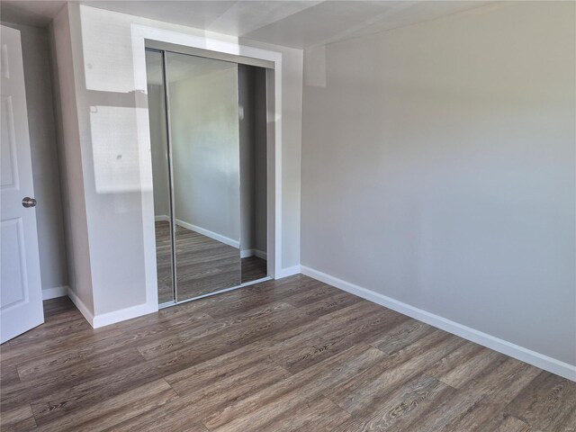 unfurnished bedroom featuring baseboards, wood finished floors, and a closet