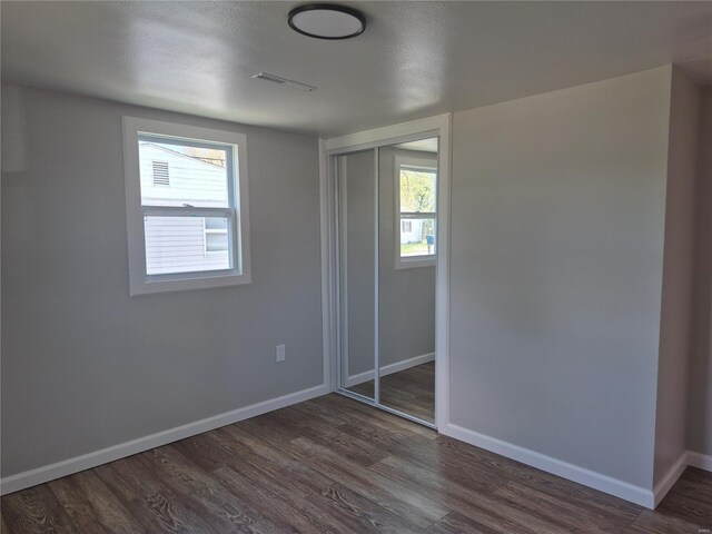 unfurnished bedroom with a closet, baseboards, dark wood-style flooring, and visible vents