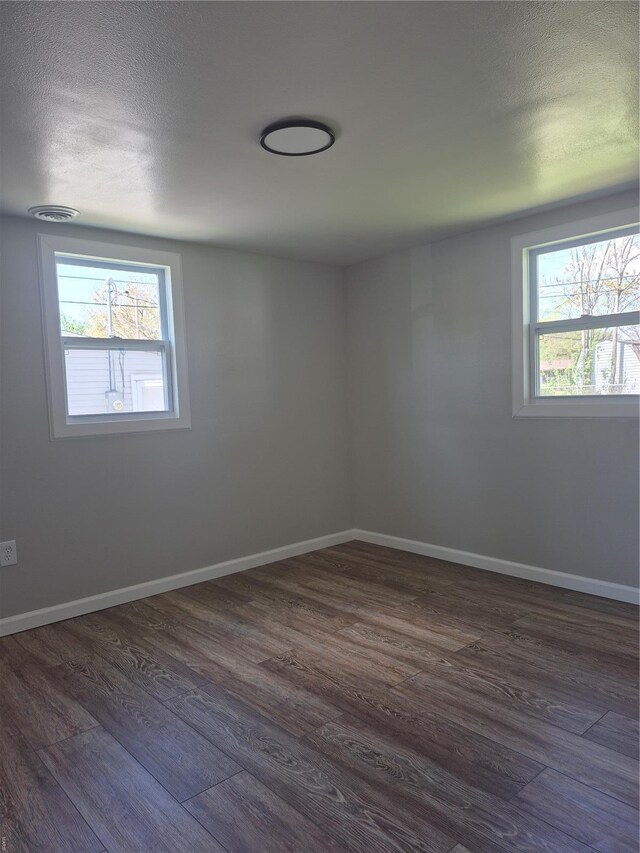 empty room featuring baseboards, a wealth of natural light, and dark wood-type flooring