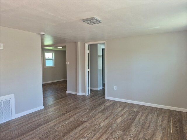 empty room with dark wood finished floors, visible vents, and baseboards