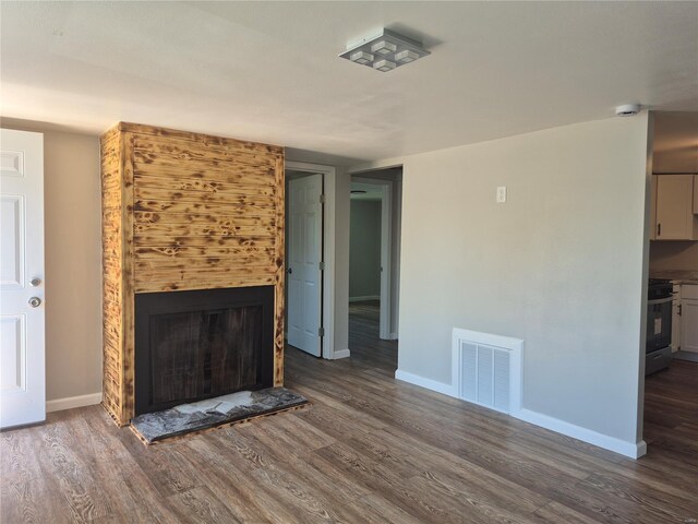unfurnished living room featuring dark wood-type flooring, visible vents, and a fireplace with raised hearth