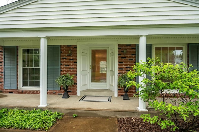 view of exterior entry with a porch and brick siding