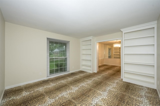 carpeted empty room with baseboards, built in features, and a chandelier