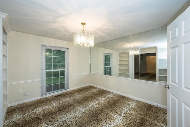 carpeted spare room with an inviting chandelier, baseboards, and built in features