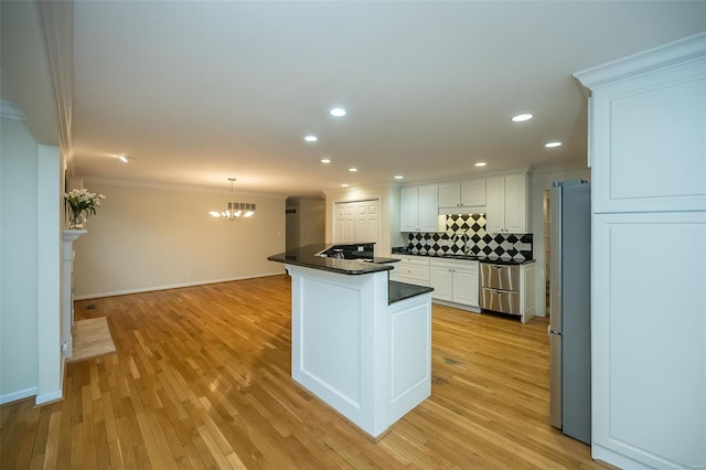 kitchen featuring dark countertops, appliances with stainless steel finishes, a chandelier, white cabinetry, and ornamental molding