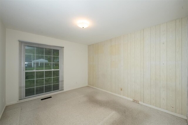 carpeted empty room with wooden walls, baseboards, and visible vents