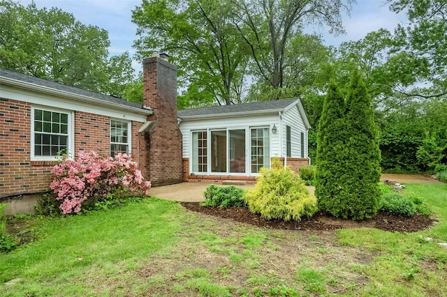 back of property featuring brick siding, a patio area, a yard, and a chimney