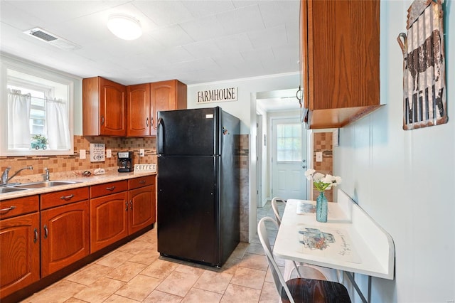 kitchen with a sink, light countertops, freestanding refrigerator, backsplash, and visible vents