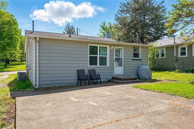 back of property with central air condition unit, a yard, and a chimney