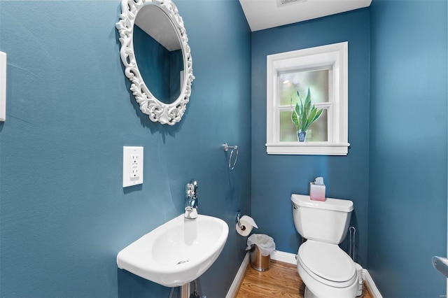 half bath with toilet, baseboards, visible vents, a sink, and wood finished floors