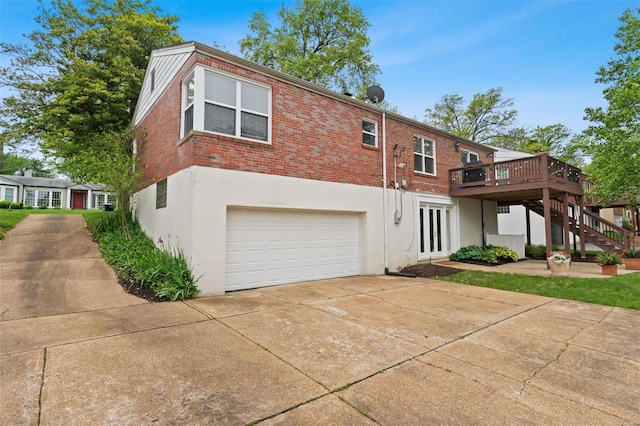 back of house featuring a deck, an attached garage, stairs, brick siding, and concrete driveway