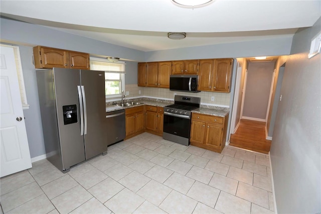 kitchen featuring a sink, brown cabinetry, backsplash, and appliances with stainless steel finishes