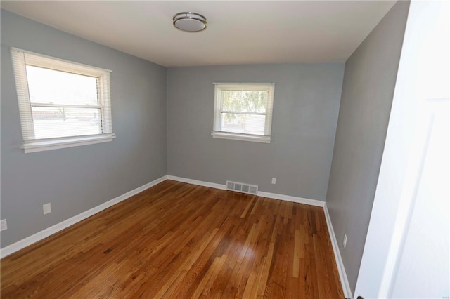 spare room with baseboards, visible vents, and wood finished floors