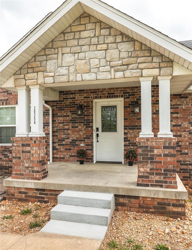 property entrance with a porch, brick siding, and stone siding