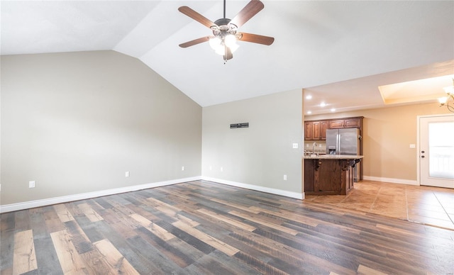 unfurnished living room with a sink, baseboards, ceiling fan with notable chandelier, and wood finished floors