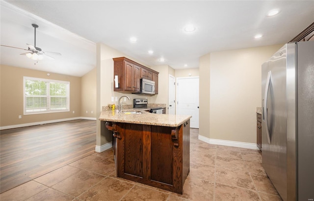 kitchen featuring appliances with stainless steel finishes, light stone counters, a sink, a peninsula, and a ceiling fan
