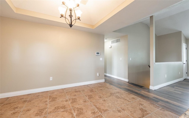 spare room featuring baseboards, visible vents, an inviting chandelier, and a raised ceiling