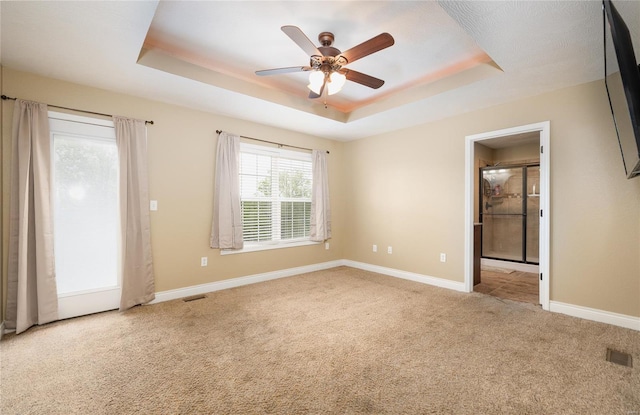 empty room featuring carpet floors, visible vents, baseboards, ceiling fan, and a raised ceiling