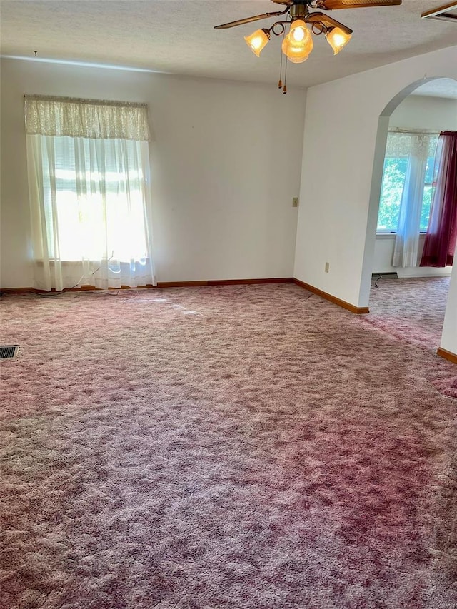 carpeted spare room with arched walkways, a textured ceiling, visible vents, baseboards, and a ceiling fan