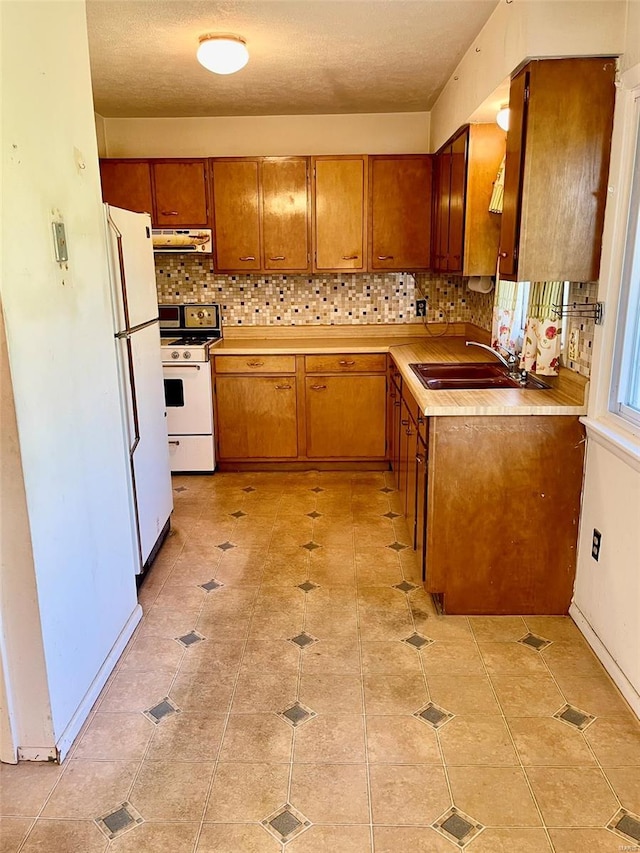 kitchen with brown cabinets, tasteful backsplash, under cabinet range hood, and white appliances