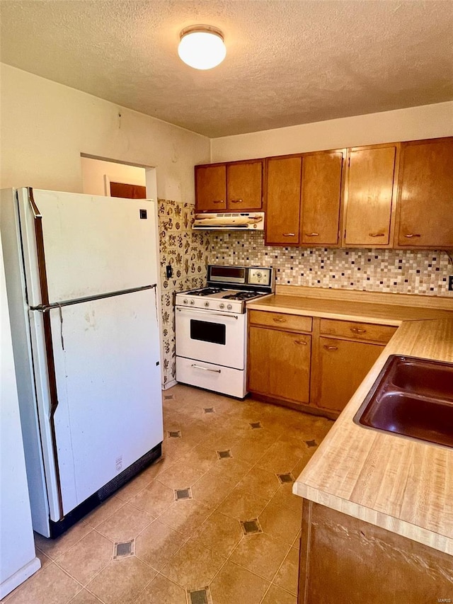 kitchen with under cabinet range hood, light countertops, a sink, white appliances, and brown cabinetry