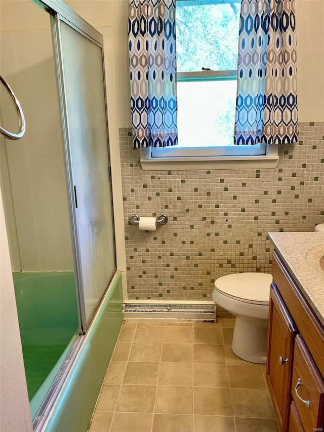 bathroom with tile patterned floors, toilet, vanity, a baseboard heating unit, and bath / shower combo with glass door