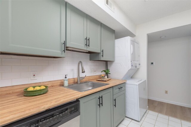 kitchen with visible vents, tasteful backsplash, stacked washer / drying machine, a sink, and dishwashing machine