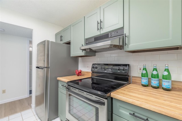 kitchen with light tile patterned flooring, stainless steel appliances, decorative backsplash, under cabinet range hood, and butcher block counters