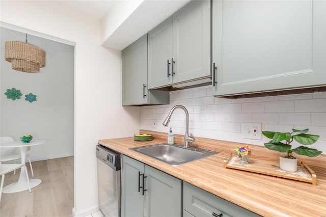 kitchen featuring baseboards, light wood-style floors, tasteful backsplash, a sink, and dishwasher