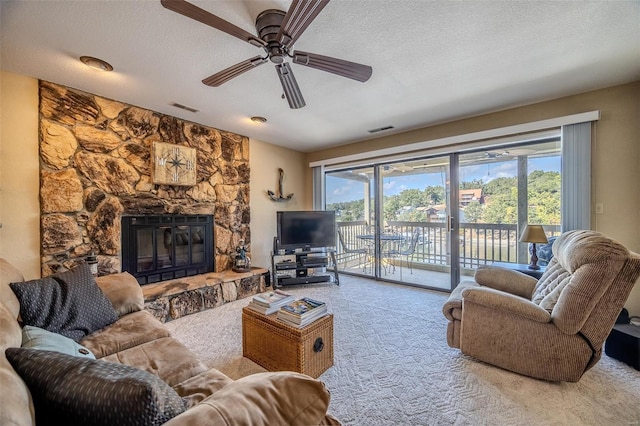 living area featuring a ceiling fan, a textured ceiling, visible vents, a fireplace, and carpet floors