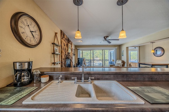 kitchen with a ceiling fan, dark countertops, hanging light fixtures, and a sink