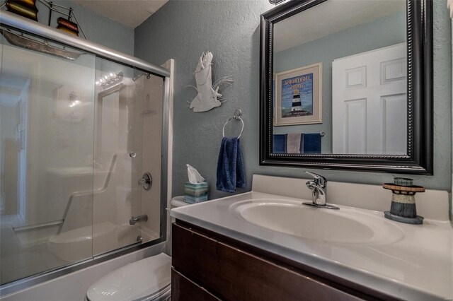 bathroom with toilet, a textured wall, shower / bath combination with glass door, and vanity