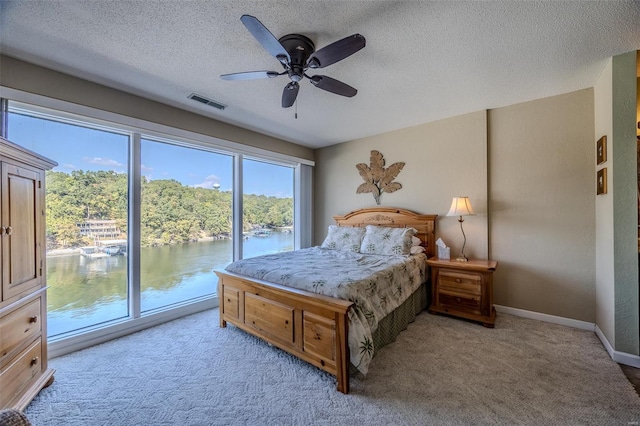 bedroom with access to outside, light carpet, a textured ceiling, a water view, and visible vents