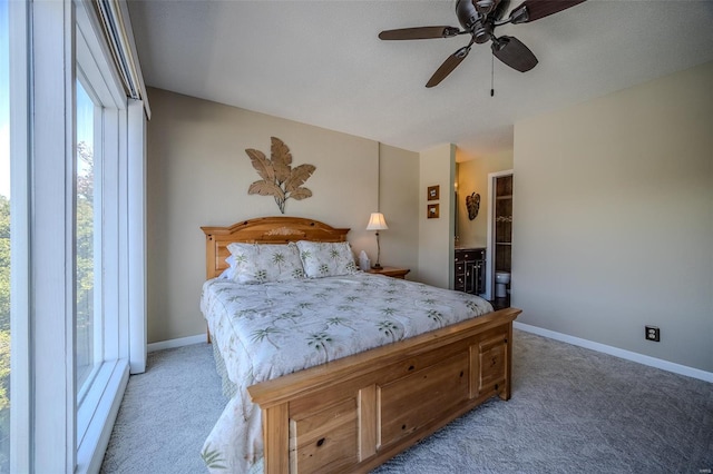 bedroom featuring connected bathroom, baseboards, light carpet, and ceiling fan