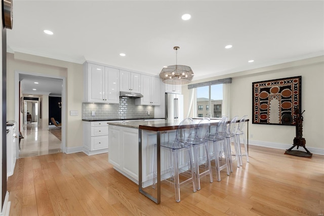 kitchen with a kitchen bar, light wood-type flooring, high end refrigerator, a chandelier, and under cabinet range hood