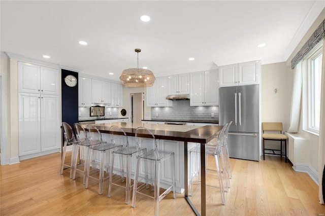 kitchen with decorative backsplash, dark countertops, high quality fridge, white cabinetry, and light wood-style flooring