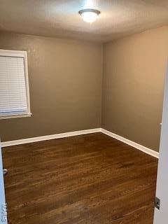 spare room with baseboards and dark wood-style flooring