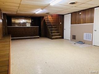 finished below grade area featuring stairway, wooden walls, visible vents, and a paneled ceiling
