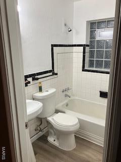 bathroom with wood finished floors, toilet, tile walls, and  shower combination